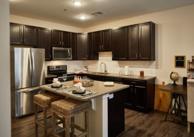 A kitchen at The Winston at Lyndhurst Apartments featuring cabinetry, stainless steel appliances, a subway tile backsplash, and an island with bar seating.