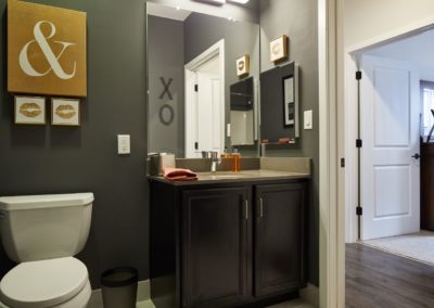 A bathroom at The Winston at Lyndhurst Apartments featuring dark cabinetry, a vanity with a large mirror, and stylish decor accents.