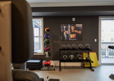 The fitness center at The Winston at Lyndhurst Apartments, featuring a rack of kettlebells, medicine balls, workout mats, and strength training equipment. A motivational fitness poster hangs on the dark accent wall.