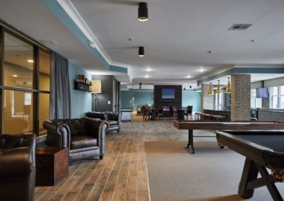 The Clubhouse at The Winston at Lyndhurst Apartments, featuring plush leather seating, a billiards table, a shuffleboard table, and a spacious entertainment area with a large TV.