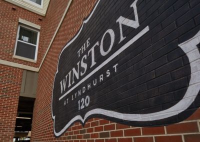 Close-up of The Winston at Lyndhurst Apartments' exterior brick wall featuring a black and white painted logo with the address number "120".