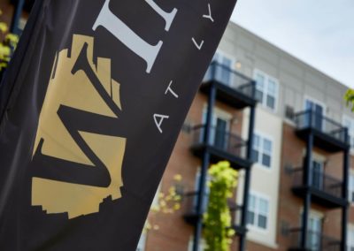 Close-up of a branded flag featuring The Winston at Lyndhurst Apartments logo, with the apartment building’s modern exterior and private balconies visible in the background.